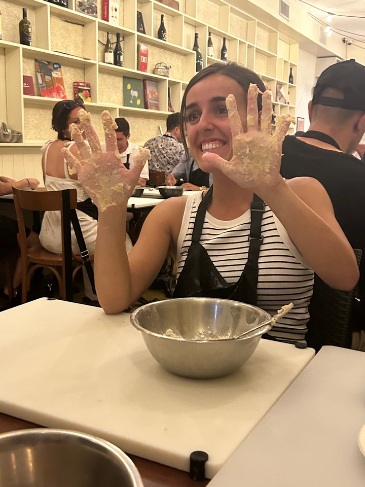 Personne avec les mains couvertes de pâte, souriante à une table avec un bol à mélanger.