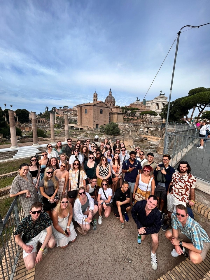 Groupe nombreux de personnes posant devant des ruines romaines antiques.