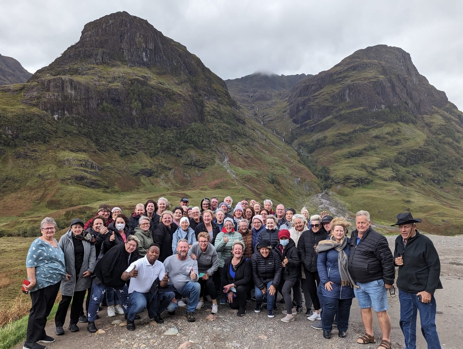 Grand groupe de personnes posant devant un paysage montagneux.