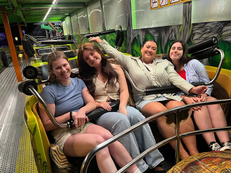 Quatre femmes assises dans un manège de parc d'attractions, souriant à la caméra.