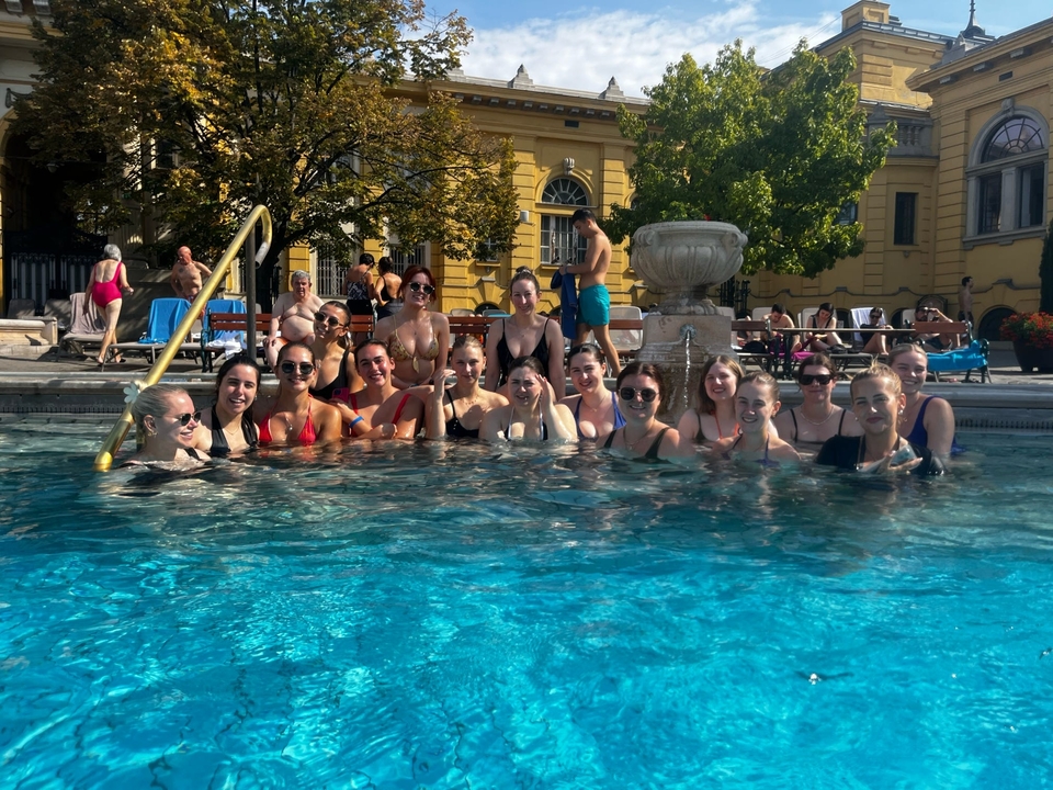 Grand groupe dans une piscine posant pour une photo, avec la façade d'un bâtiment historique en arrière-plan.