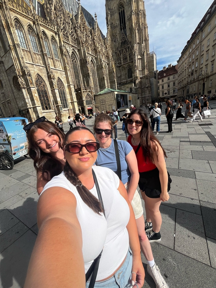 Quatre amis prenant un selfie sur une place de ville européenne.