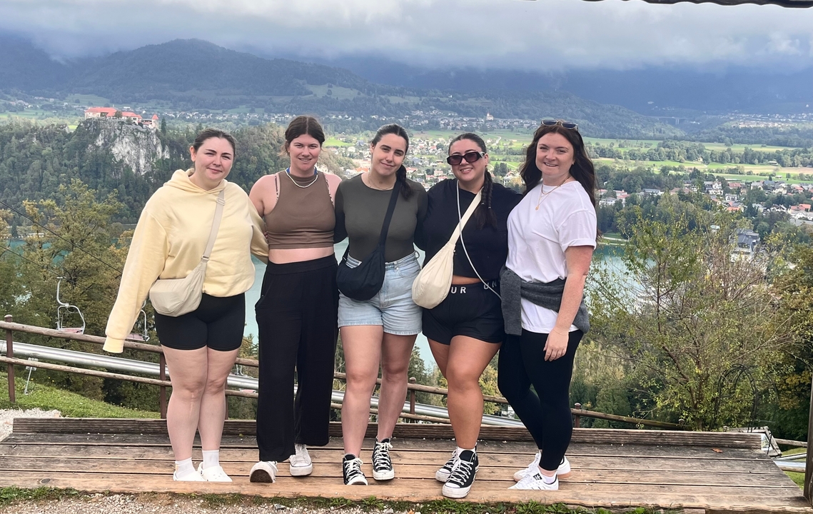Cinq femmes posant avec une vue panoramique sur des montagnes et un lac.