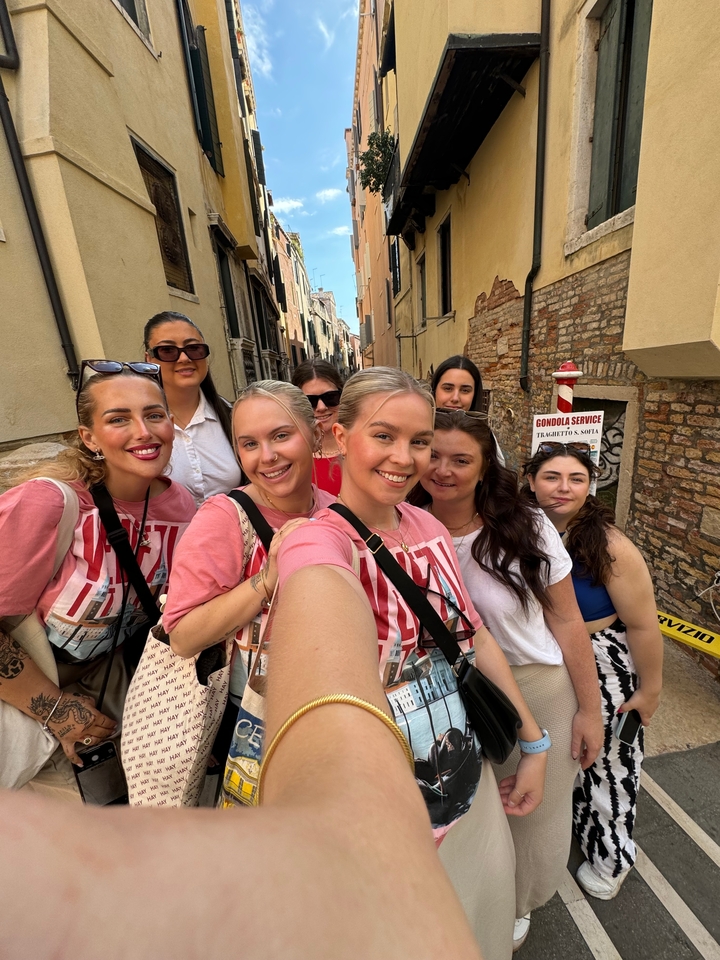 Selfie de groupe dans une rue étroite avec un panneau de service de gondole visible.
