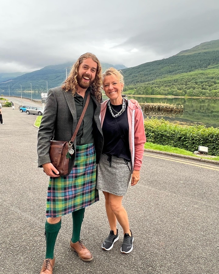 Deux personnes souriantes, une portant un kilt, avec un paysage de campagne hivernale en arrière-plan.