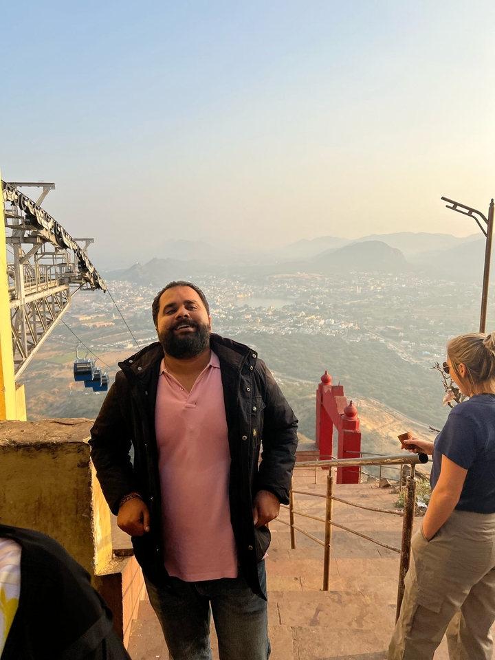 Un homme souriant avec une vue aérienne panoramique d'une ville et de montagnes en arrière-plan.