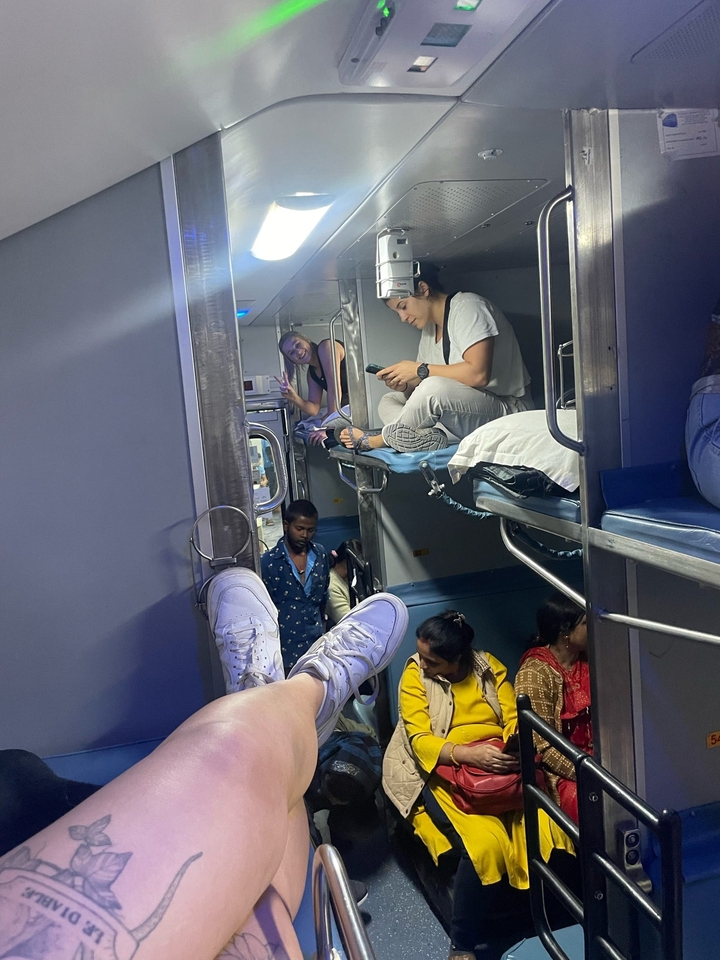 Des personnes assises et allongées dans un compartiment de train avec des lits superposés.