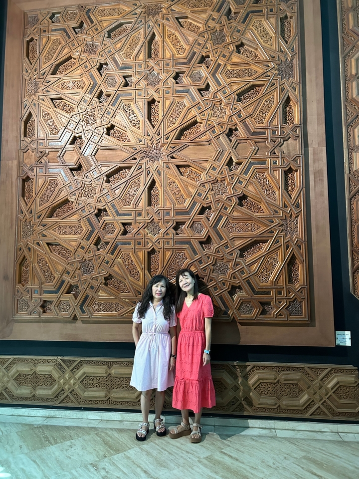 Deux personnes souriantes devant une sculpture en bois complexe.