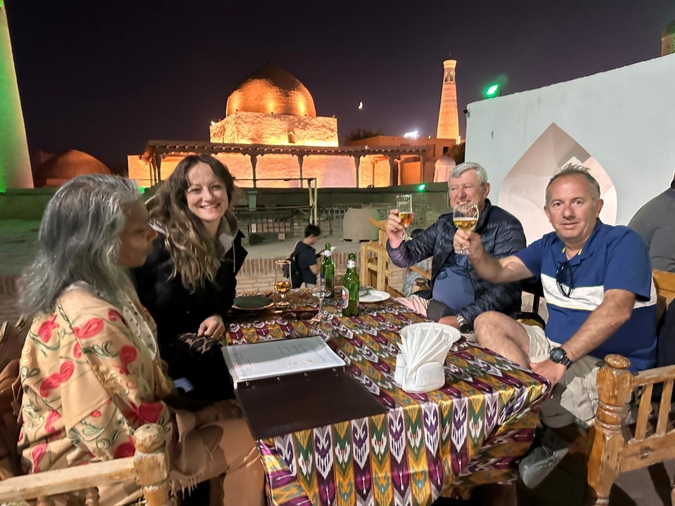 Personas cenando al aire libre por la noche con un edificio histórico al fondo.