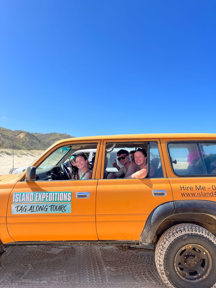 Des gens dans un véhicule sur une plage de sable avec des montagnes en arrière-plan.