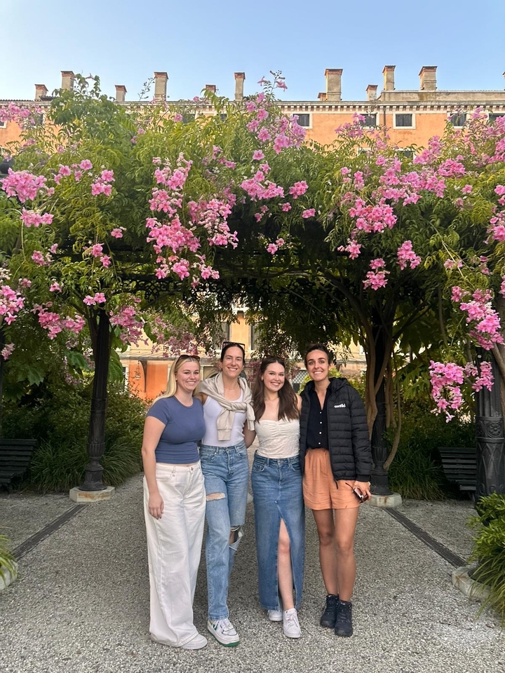Quatre femmes souriantes sous une arche florale.