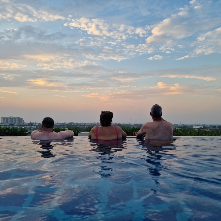 Trois personnes dans une piscine avec vue sur un paysage urbain.