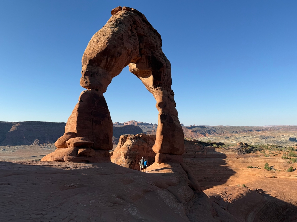 Deux personnes se tenant debout sous la grande arche de pierre formée naturellement.