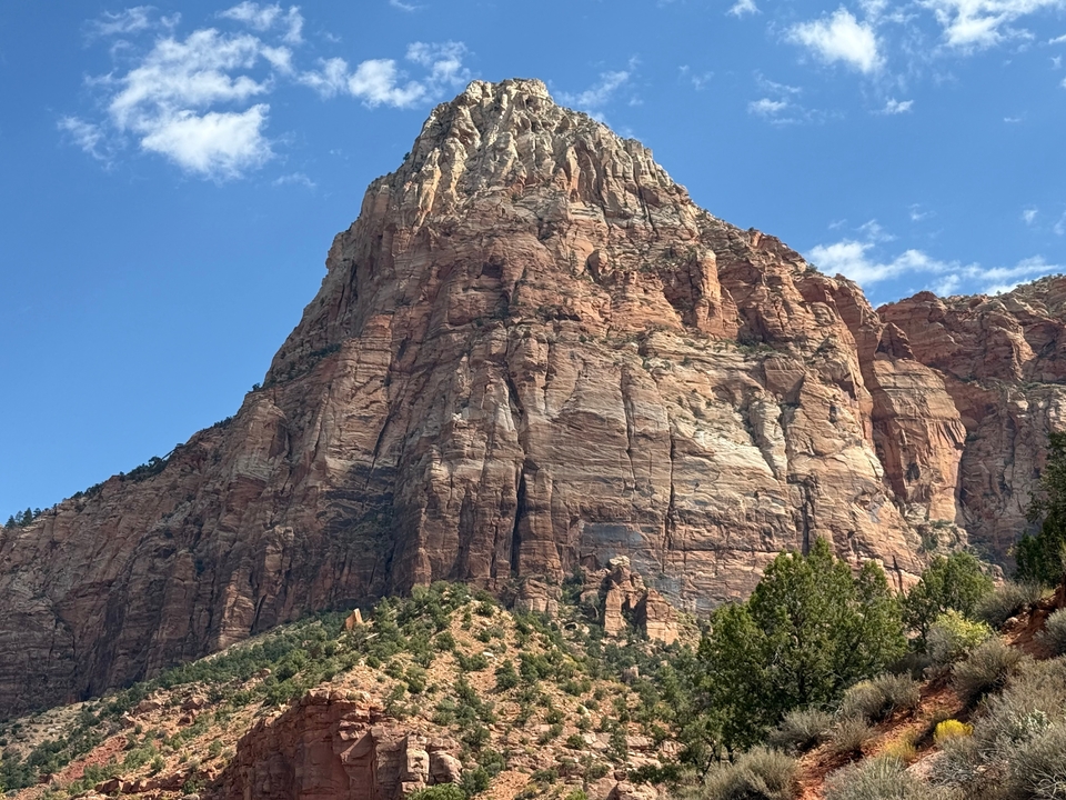 Une imposante formation rocheuse rouge se dressant contre un ciel bleu dégagé avec de la végétation visible au premier plan.