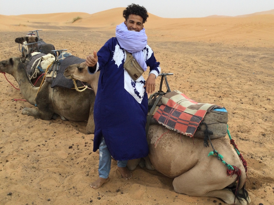 Homme avec des chameaux dans le désert, vêtu d'un habit traditionnel.