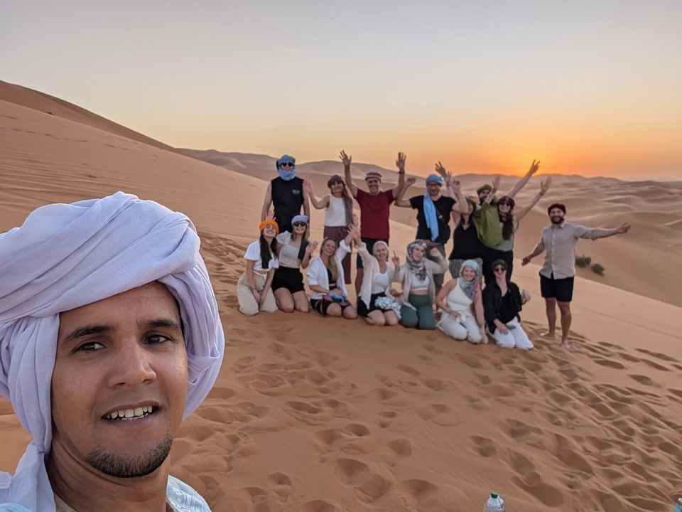 Gruppe von Menschen in der Wüste bei Sonnenuntergang mit Dünen im Hintergrund.
