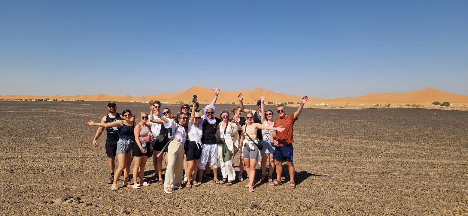 Gruppe von Menschen, die vor Sanddünen unter einem klaren blauen Himmel posieren.
