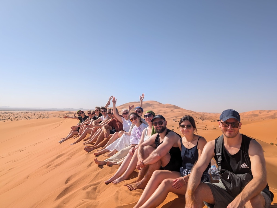 Gruppe von Menschen, die auf einer Sanddüne in einer Wüstenlandschaft sitzen.