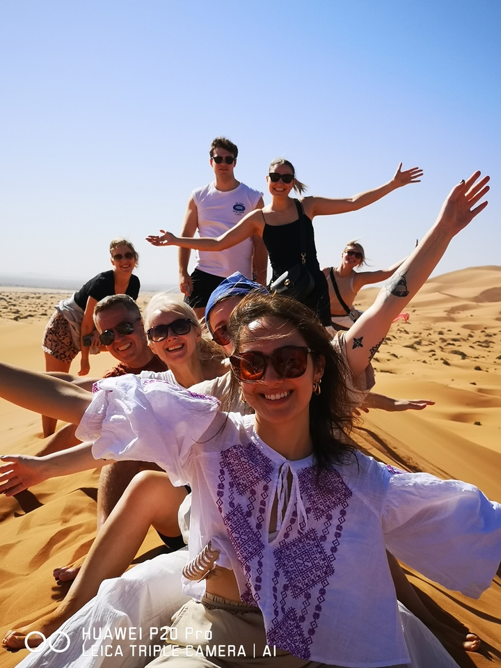 Nahaufnahme einer Gruppe lächelnder Menschen mit Sanddünen im Hintergrund.