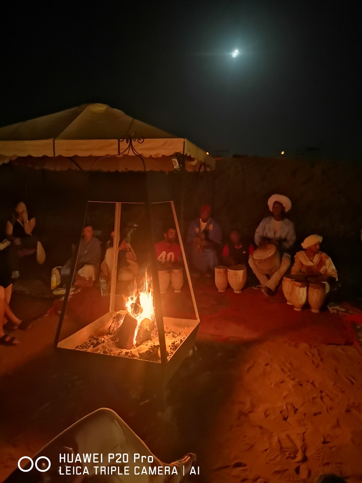 Menschen, die um ein Lagerfeuer sitzen mit Trommeln in einer schwach beleuchteten Umgebung.