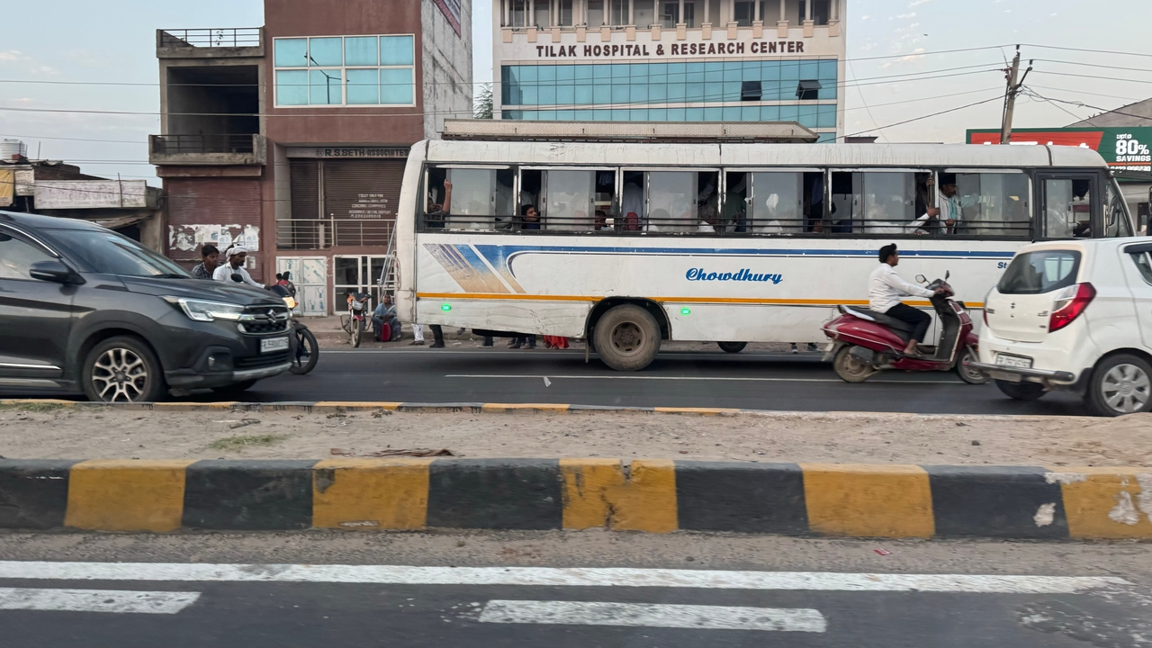 Rue de ville avec circulation incluant des bus et des scooters.