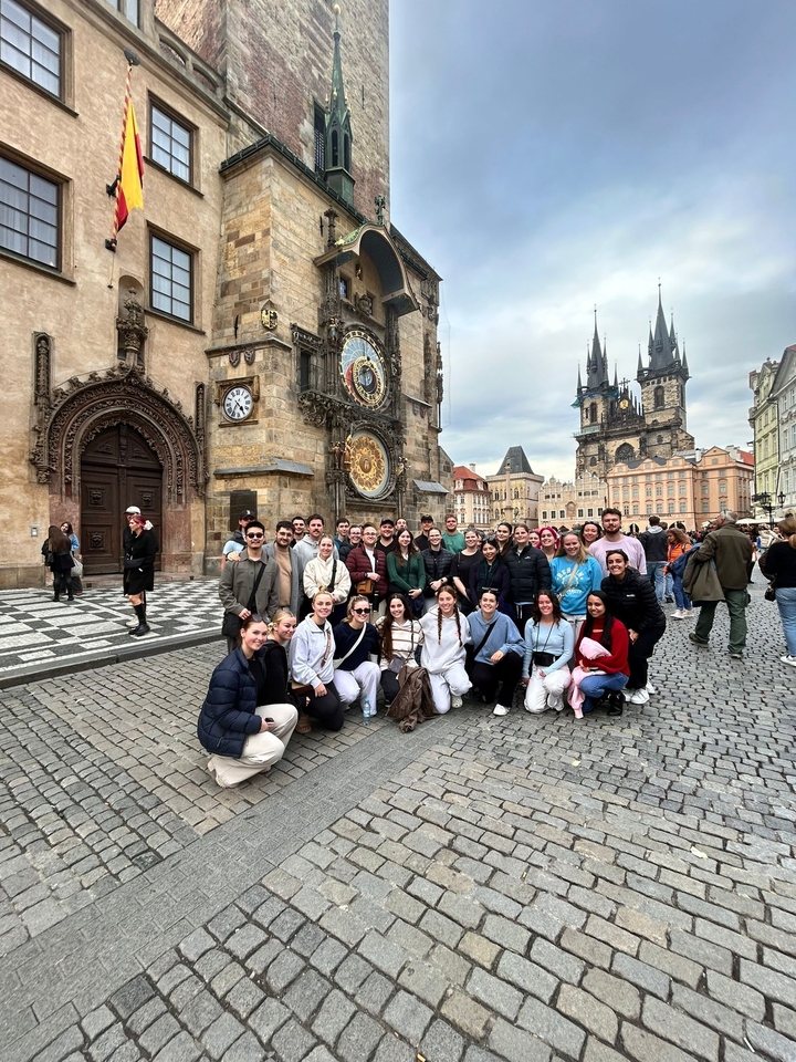 Grand groupe posant devant une horloge astronomique complexe sur un bâtiment.