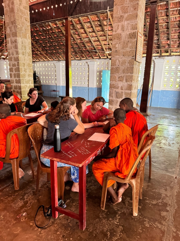 Groupe de personnes interagissant avec des moines assis à une table.
