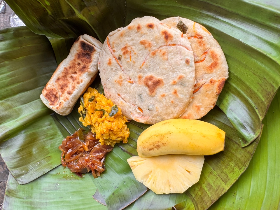 Repas traditionnel sur feuilles de bananier comprenant du pain et des fruits.