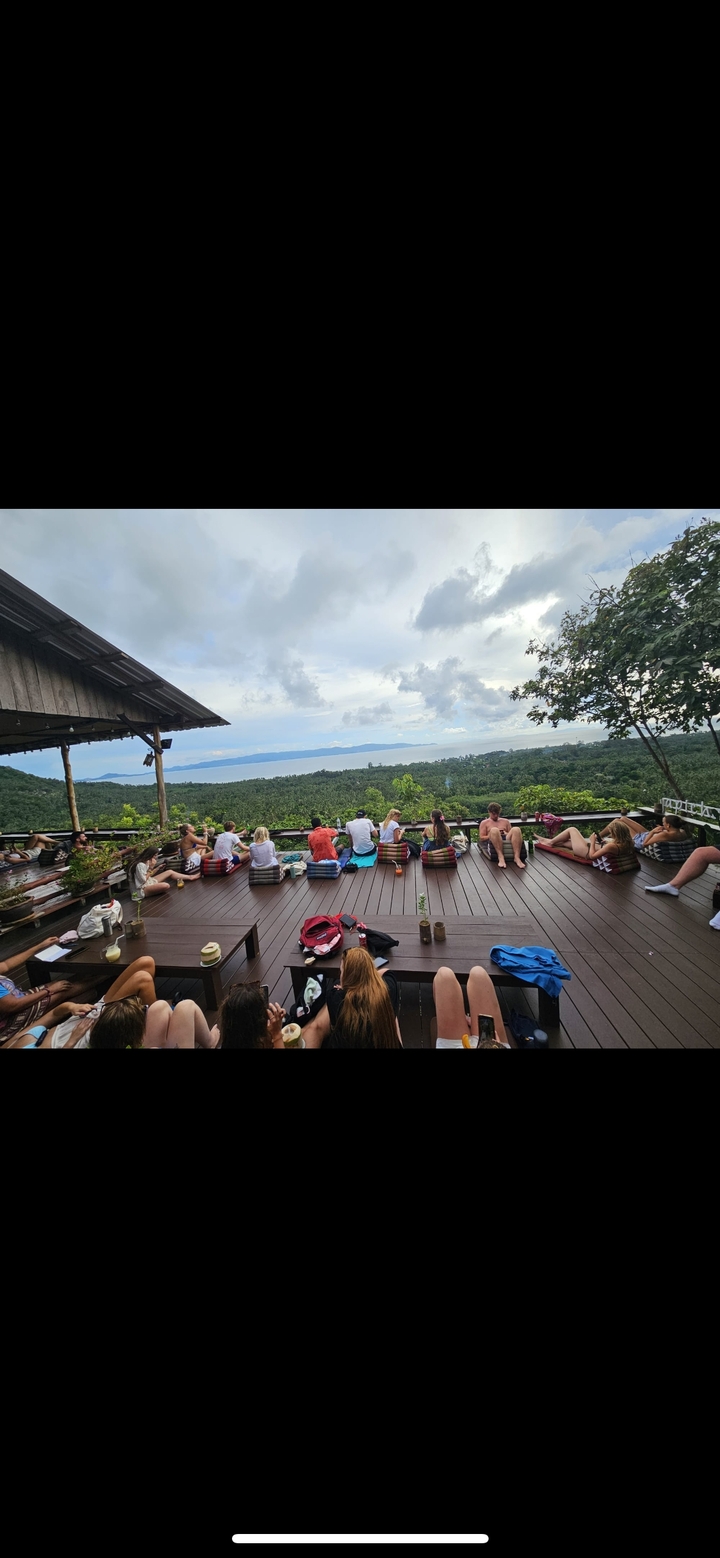 Des gens se détendant sur une terrasse avec une vue panoramique sur une forêt et la mer.