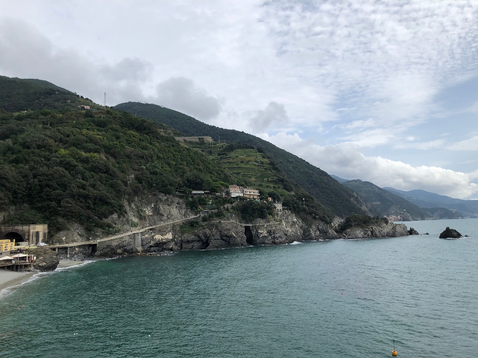 Vue côtière avec collines et bâtiments au bord de la mer sous un ciel nuageux.