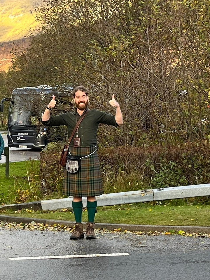 Personne qui pose avec les deux pouces levés devant des buissons.
