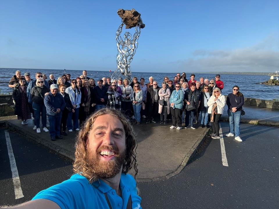 Groupe de personnes posant devant une grande sculpture près de l'eau.