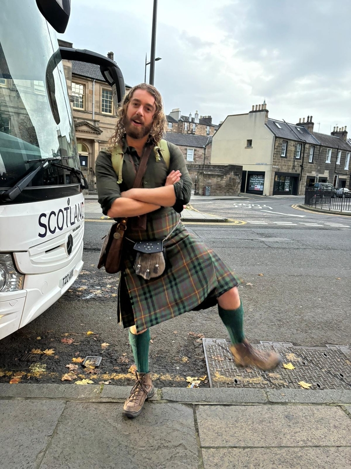 Homme posant en tenue écossaise traditionnelle devant un bus.