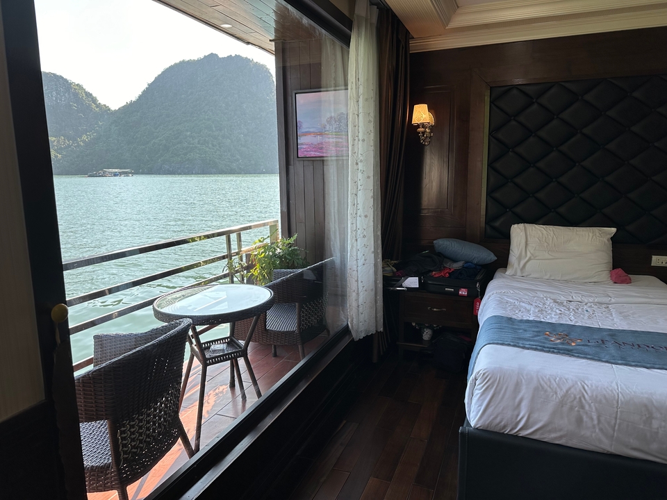 Cozy cruise cabin with bed and balcony overlooks serene emerald waters and limestone karst peaks.