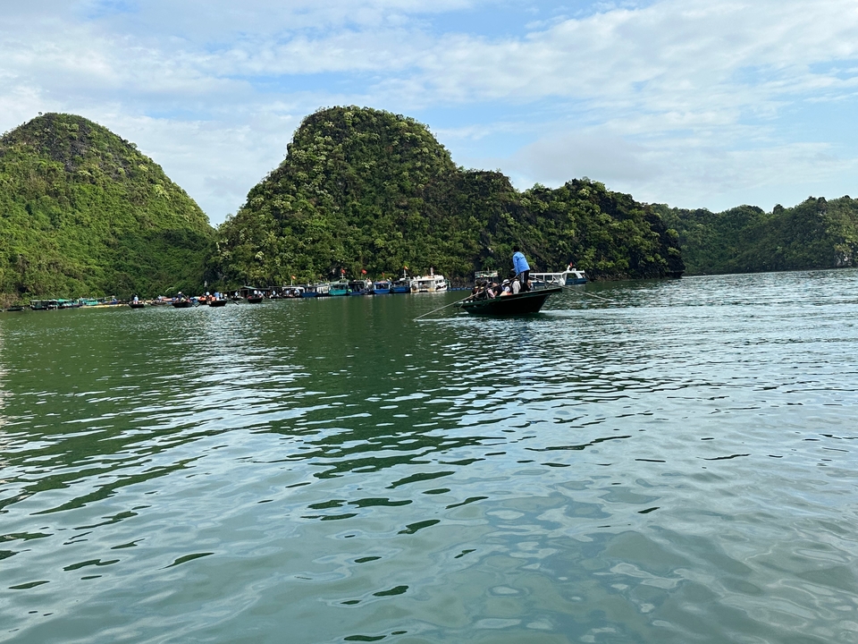 Small fishing boat glides across calm green waters surrounded by jungle-clad limestone islands.
