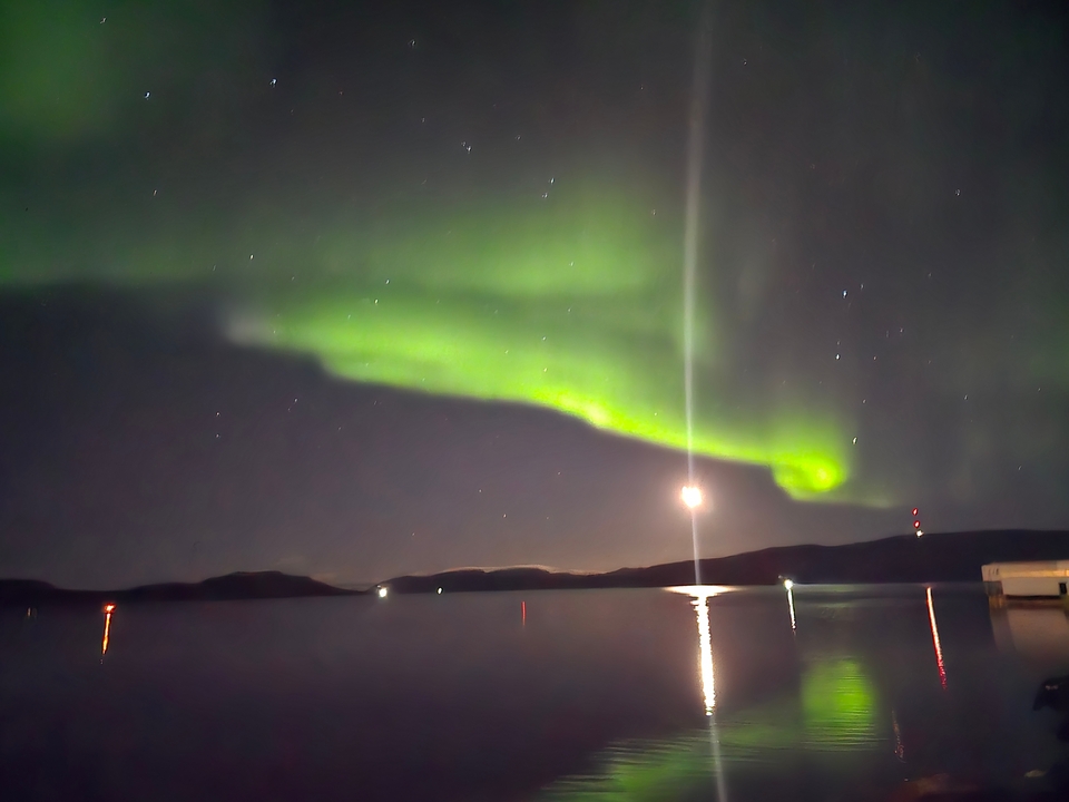 Aurores boréales au-dessus de l'eau avec la lune et des structures.