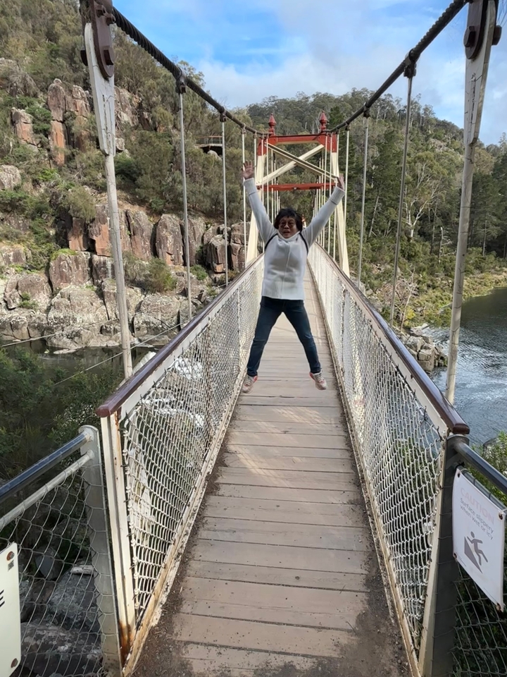 Personne sautant sur un pont suspendu au-dessus d'une rivière.