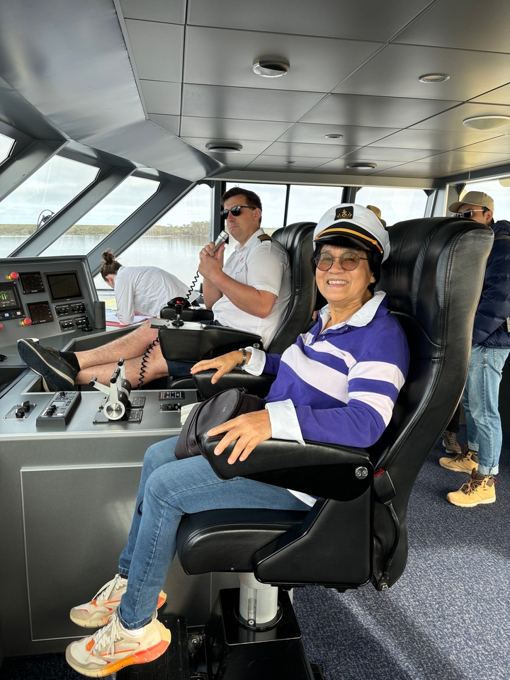 Une personne à la barre d'un navire avec des membres d'équipage autour.