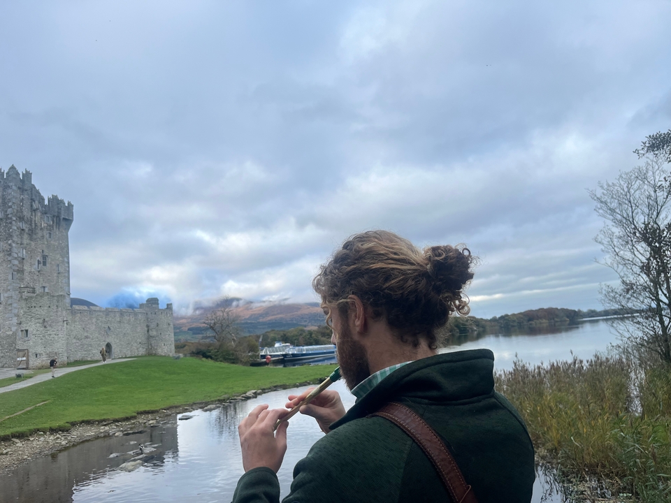 Mann spielt ein Musikinstrument bei einem Schloss am Seeufer.