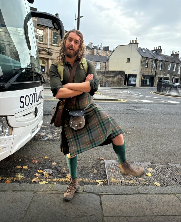 Homme portant un kilt posant devant un autocar de tourisme.