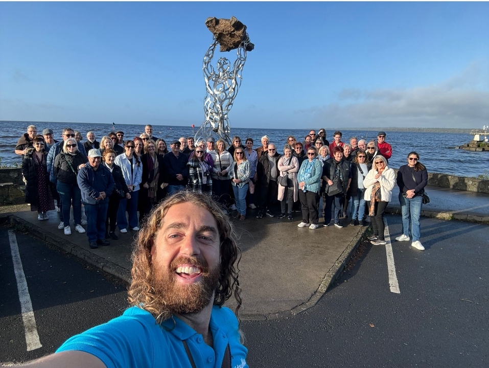 Grand groupe posant près d'une sculpture au bord d'un plan d'eau.