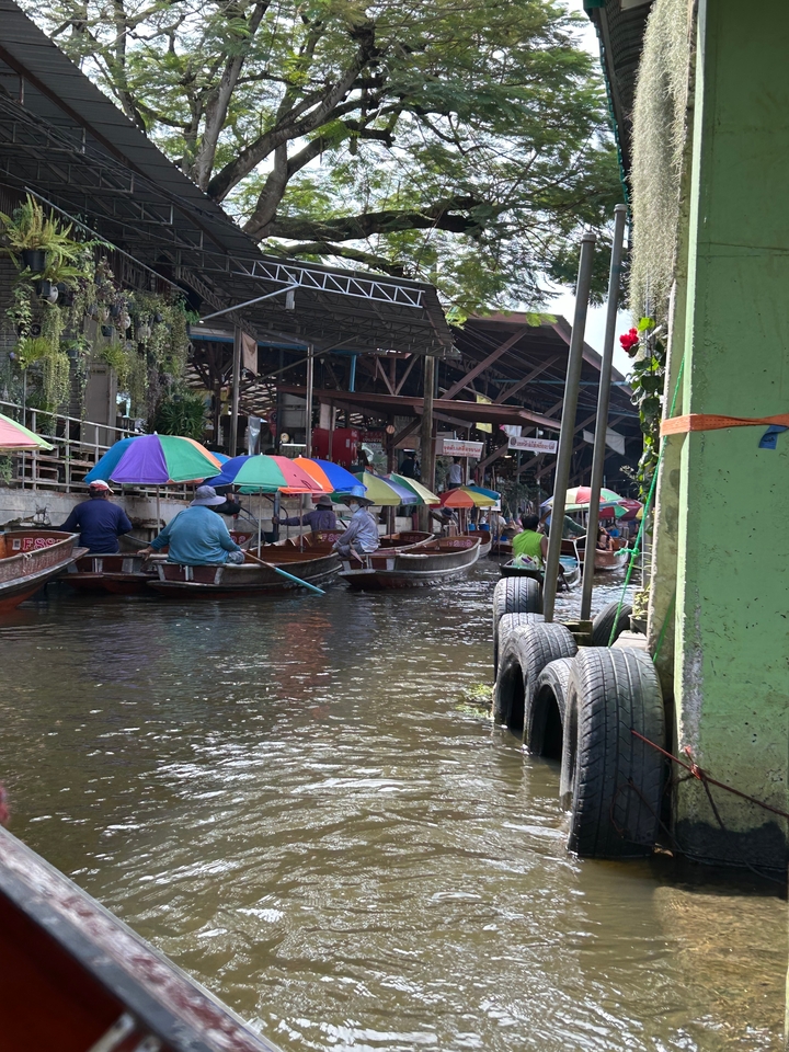 Marché flottant avec plusieurs parasols colorés et des gens ramant dans des bateaux sur un canal.