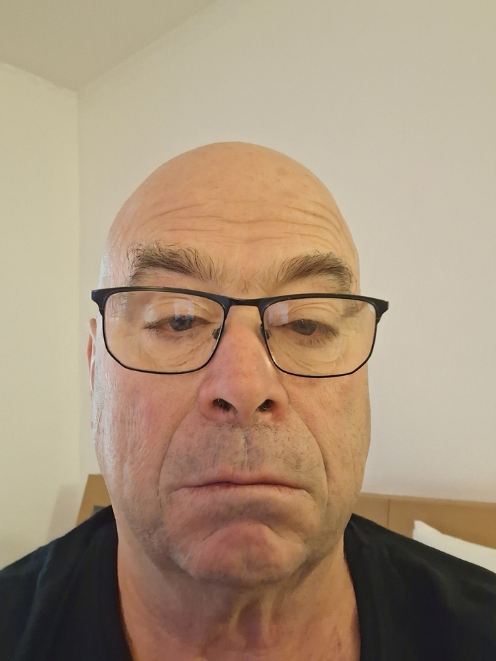 Plan rapproché d'un homme portant des lunettes à l'intérieur avec un arrière-plan uni.