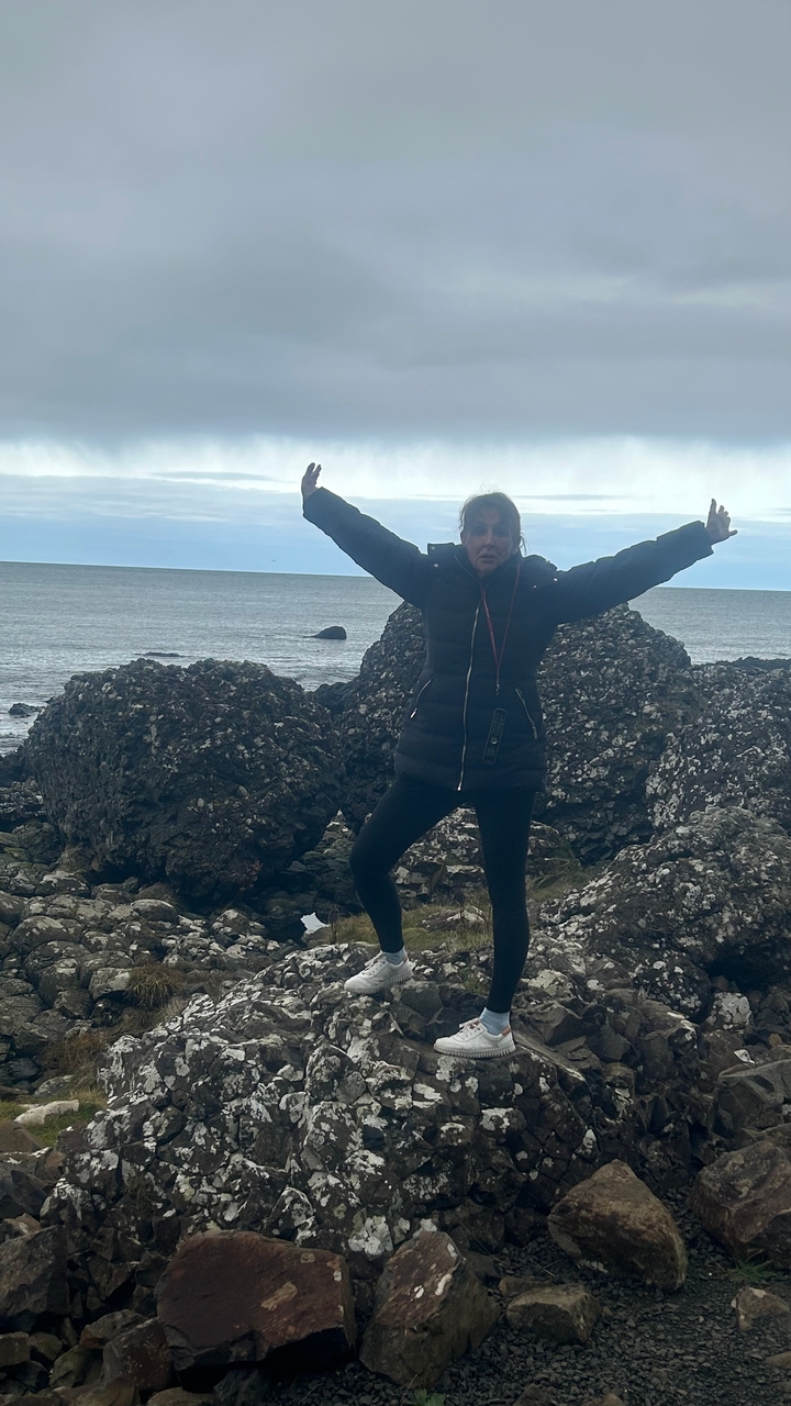 Frau, die verspielt an einer felsigen Küste am Meer posiert.