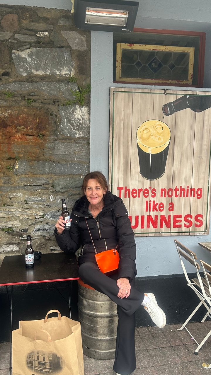 Frau sitzt an einem Tisch und hält eine Bierflasche neben einem Guinness-Schild.