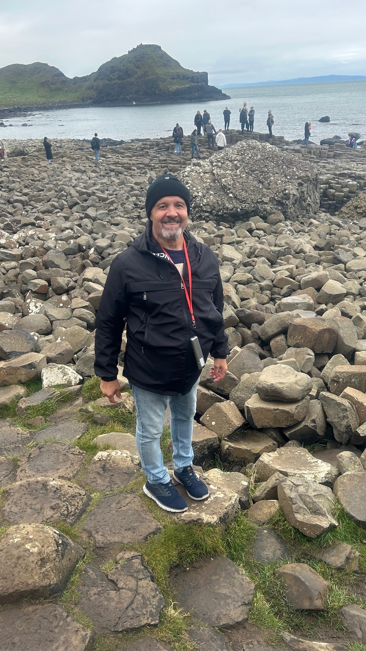 Mann posiert an einem felsigen Strand, trägt eine Jacke und blickt in die Kamera.
