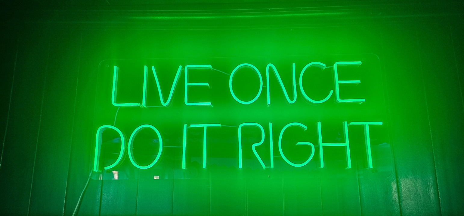 Enseigne au néon verte avec la phrase 'VIVRE UNE FOIS BIEN LE FAIRE'.