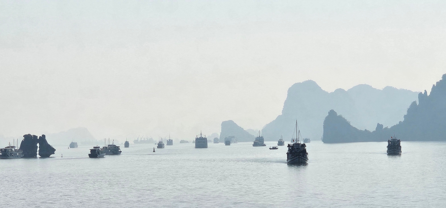 Vue majestique de bateaux sur une mer brumeuse avec des formations karstiques en arrière-plan.