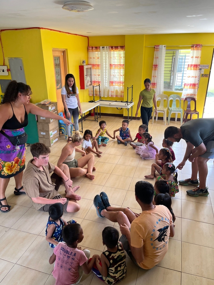 Groupe de personnes assises par terre, interagissant avec des enfants dans une salle de classe.