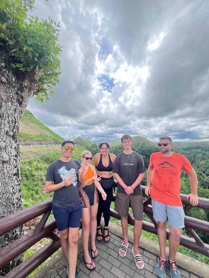 Groupe de personnes posant sur une colline avec une vue panoramique sur des monticules verdoyants et le ciel.